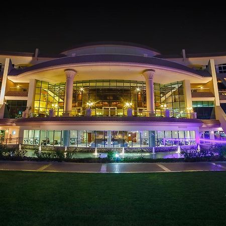 Al Raha Beach Resort & Spa Abu Dhabi Eksteriør bilde The photo shows a modern architectural building illuminated at night. The structure has a large central entrance with multiple glass windows, flanked by symmetrical columns. The exterior features a combination of sleek lines and curves, with lighting