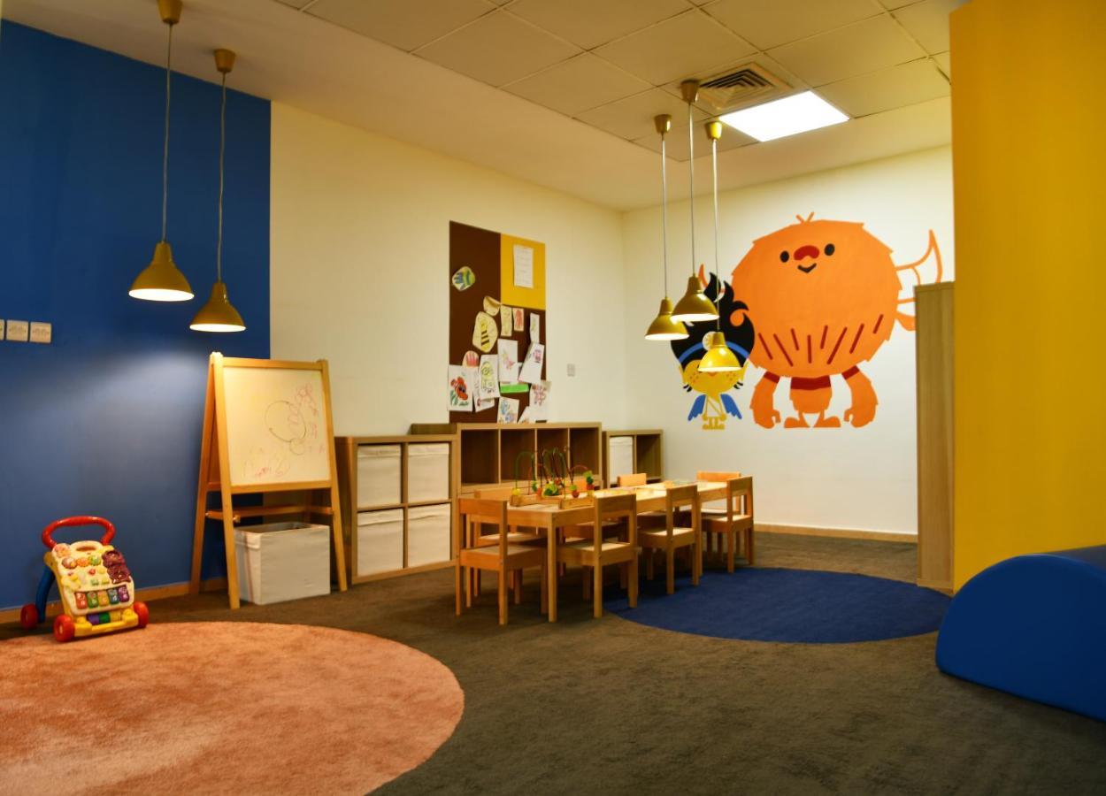 Al Raha Beach Resort & Spa Abu Dhabi Eksteriør bilde The photo shows a colorful children's classroom or play area. The walls are painted in various shades, including blue and yellow. There is a large, playful character mural on one wall that appears to be a friendly monster. 

In the room, there is a s