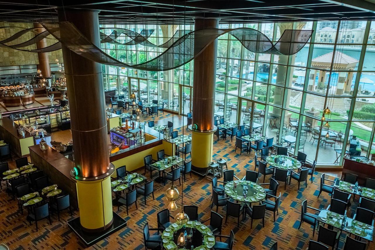 Al Raha Beach Resort & Spa Abu Dhabi Eksteriør bilde The photo shows the interior of a restaurant with a modern design. It features large windows allowing natural light to flood the space, creating an inviting atmosphere. The dining area is furnished with round tables covered with green tablecloths and