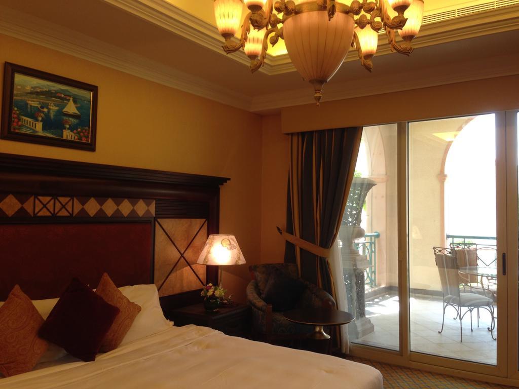 Al Raha Beach Resort & Spa Abu Dhabi Eksteriør bilde The photo shows the interior of a hotel room. The room features a large bed with decorative cushions and a wooden headboard. There's a bedside lamp emitting a warm light, and a painting is hung on the wall above the bed. To the right, there's a windo