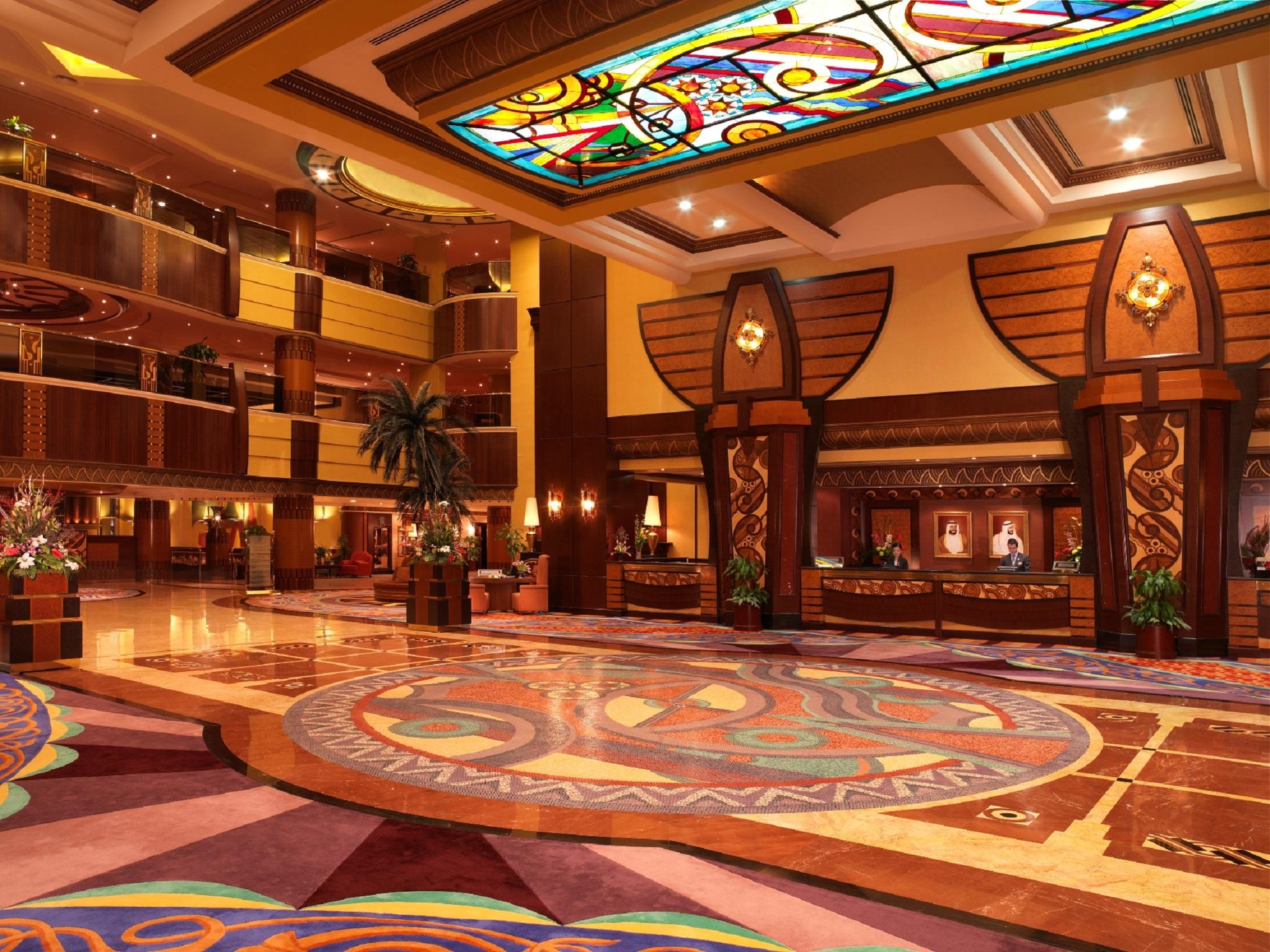 Al Raha Beach Resort & Spa Abu Dhabi Interiør bilde The photo depicts an elegantly designed hotel lobby. It features a grand ceiling with intricate stained glass and decorative patterns. The floor is adorned with colorful, ornate designs, including circular patterns. The lobby is spacious, with wooden