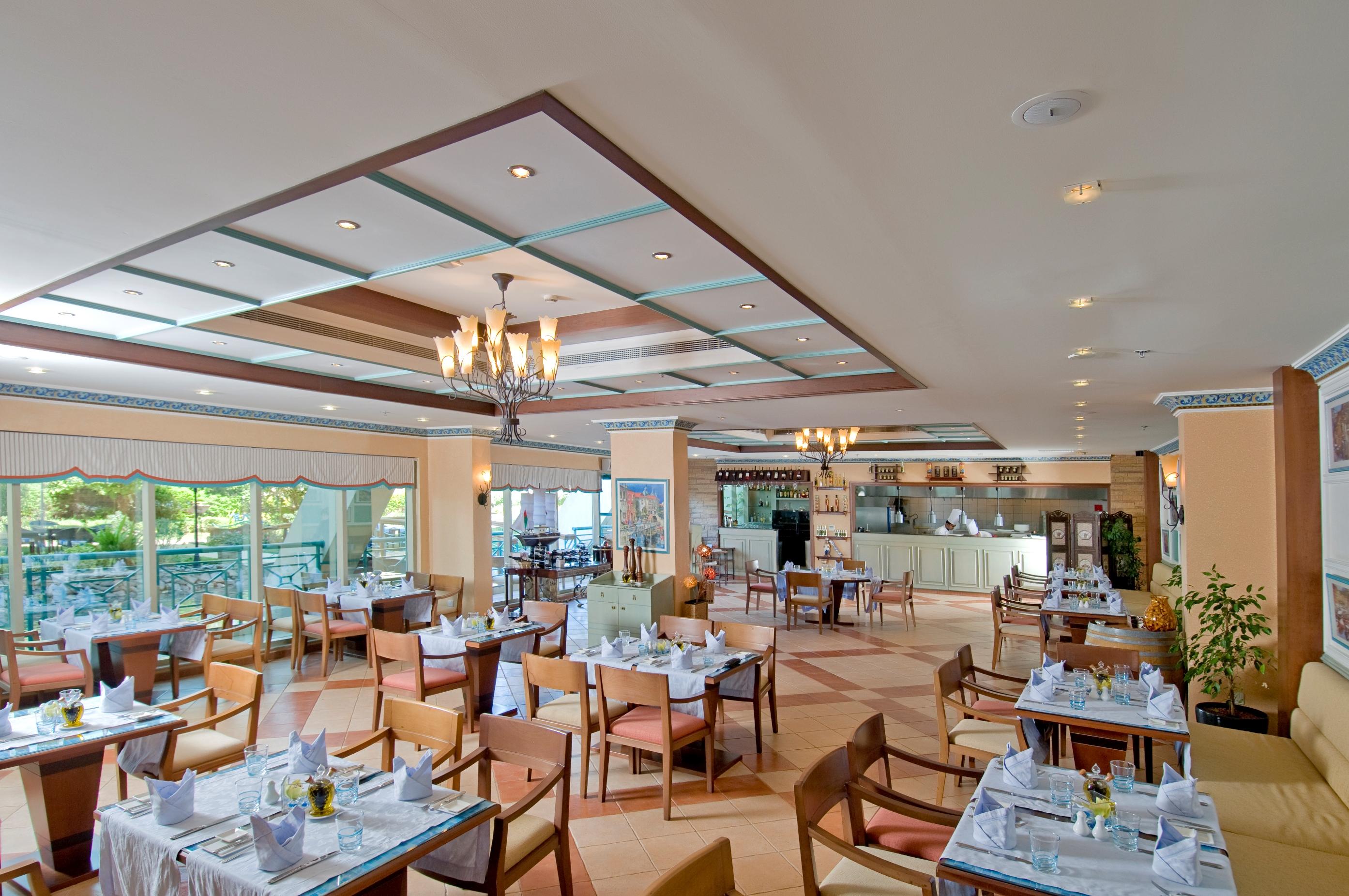Al Raha Beach Resort & Spa Abu Dhabi Restaurant bilde The photo shows the interior of a restaurant. It features a spacious dining area with multiple tables neatly arranged, each set with tableware and cloth napkins. The decor includes a decorative ceiling with lighting fixtures, and large windows that p