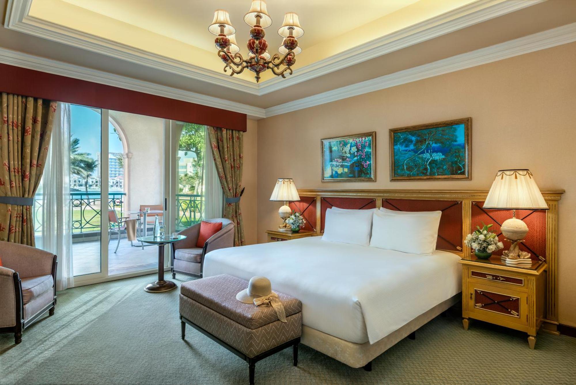 Al Raha Beach Resort & Spa Abu Dhabi Eksteriør bilde The image depicts a well-furnished hotel room. It features a large bed with white linens, flanked by two bedside lamps. Above the bed, there are two pieces of artwork hanging on the walls. To the side, there is a comfortable armchair and a small tabl