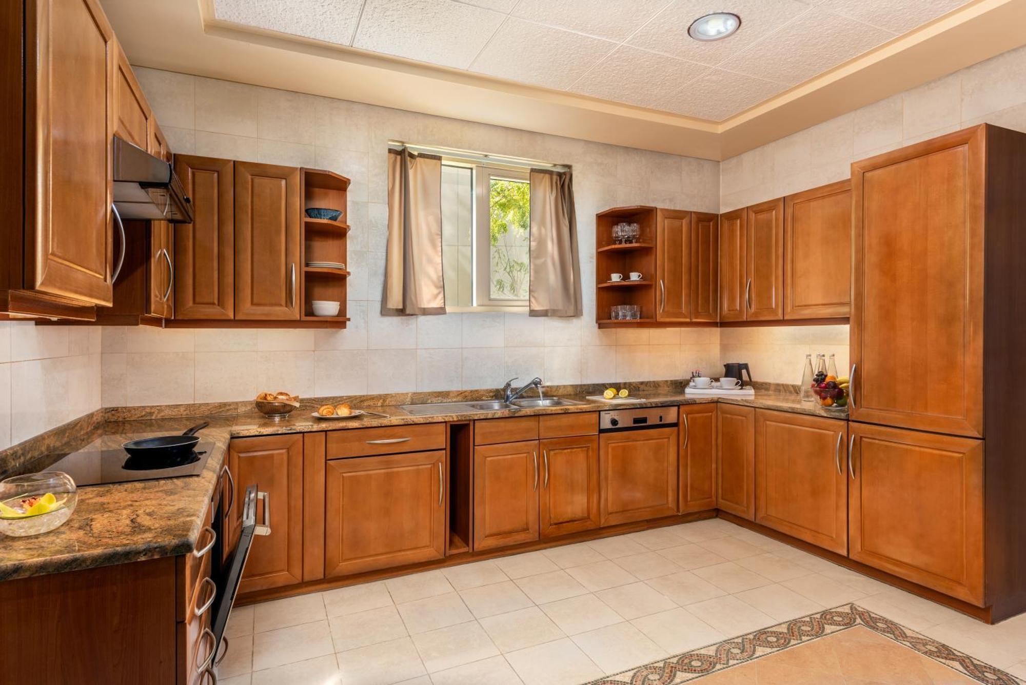 Al Raha Beach Resort & Spa Abu Dhabi Eksteriør bilde The photo shows a cozy kitchen featuring wooden cabinets with a rich brown finish, providing a warm and inviting atmosphere. The countertops are made of a light-colored stone, complementing the cabinetry. There is a window above the sink, allowing na