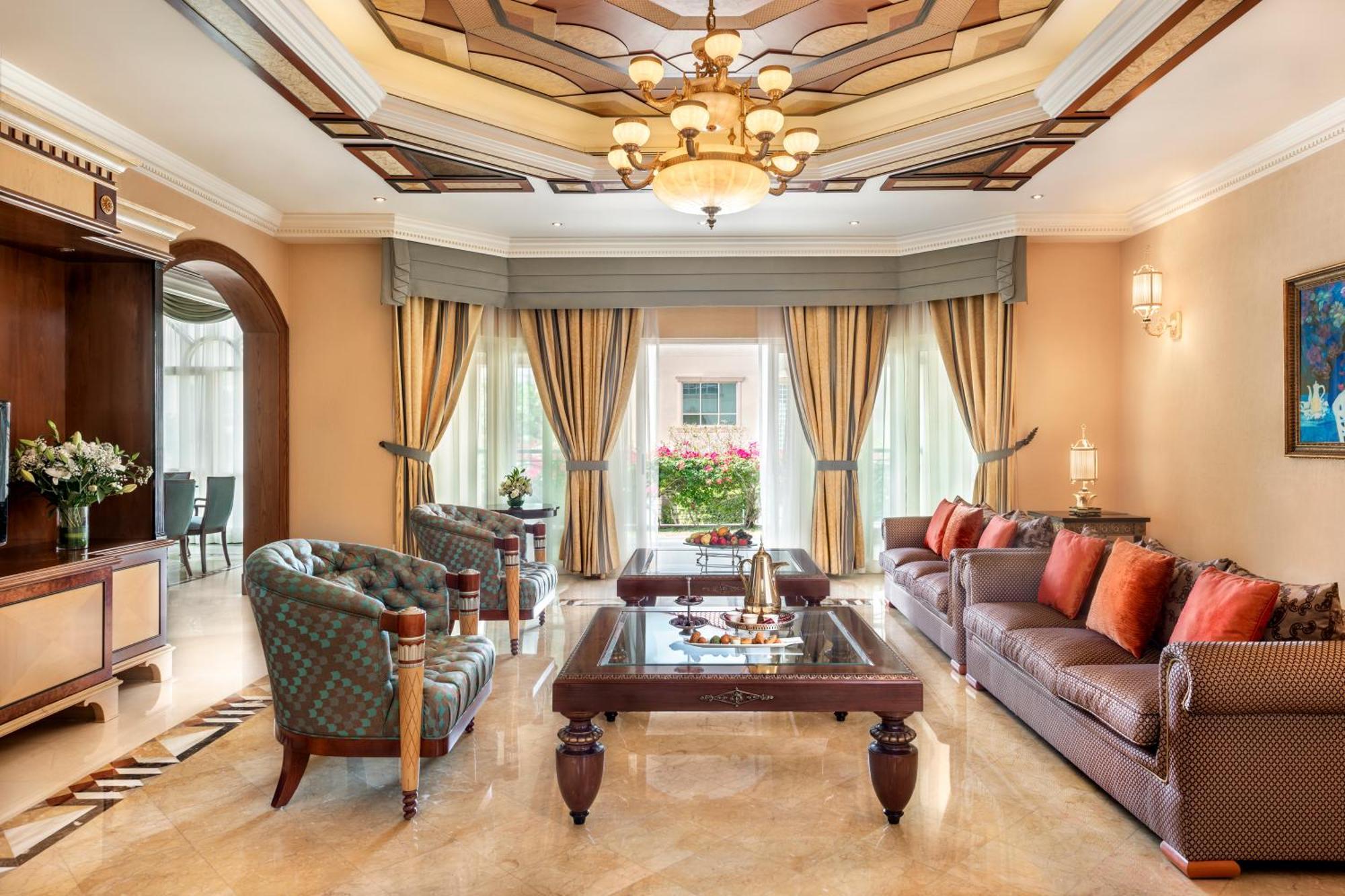 Al Raha Beach Resort & Spa Abu Dhabi Eksteriør bilde The photo shows an elegantly designed living room. It features a high, intricately patterned ceiling with a chandelier hanging in the center. The room is filled with natural light from large windows covered with flowing curtains. 

There are two diff