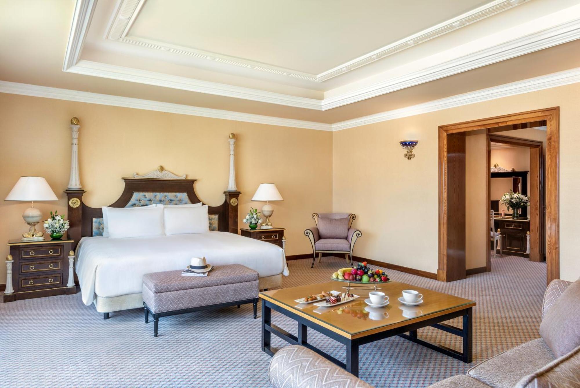 Al Raha Beach Resort & Spa Abu Dhabi Eksteriør bilde The photo shows an elegant hotel room, featuring a large bed with white linens, flanked by stylish bedside tables and lamps. The room has a warm color palette, with light brown walls and a plush carpet. A comfortable armchair is positioned nearby, an