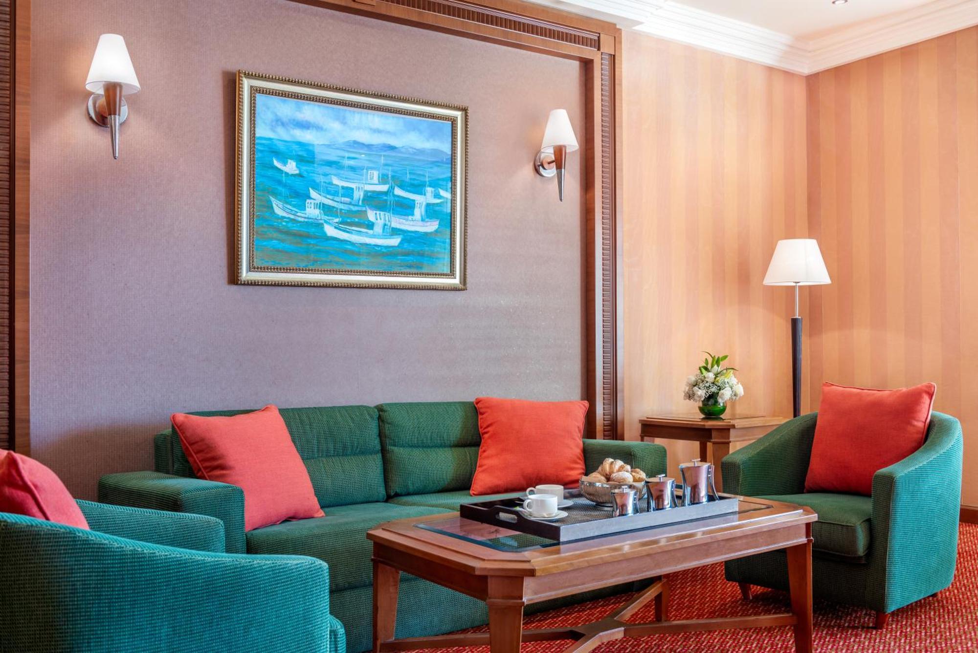 Al Raha Beach Resort & Spa Abu Dhabi Eksteriør bilde The photo displays a cozy and elegantly furnished living area. It features a green sofa adorned with orange cushions and two matching green armchairs. A wooden coffee table sits in the center, which holds a tray with beverages and snacks. The walls a
