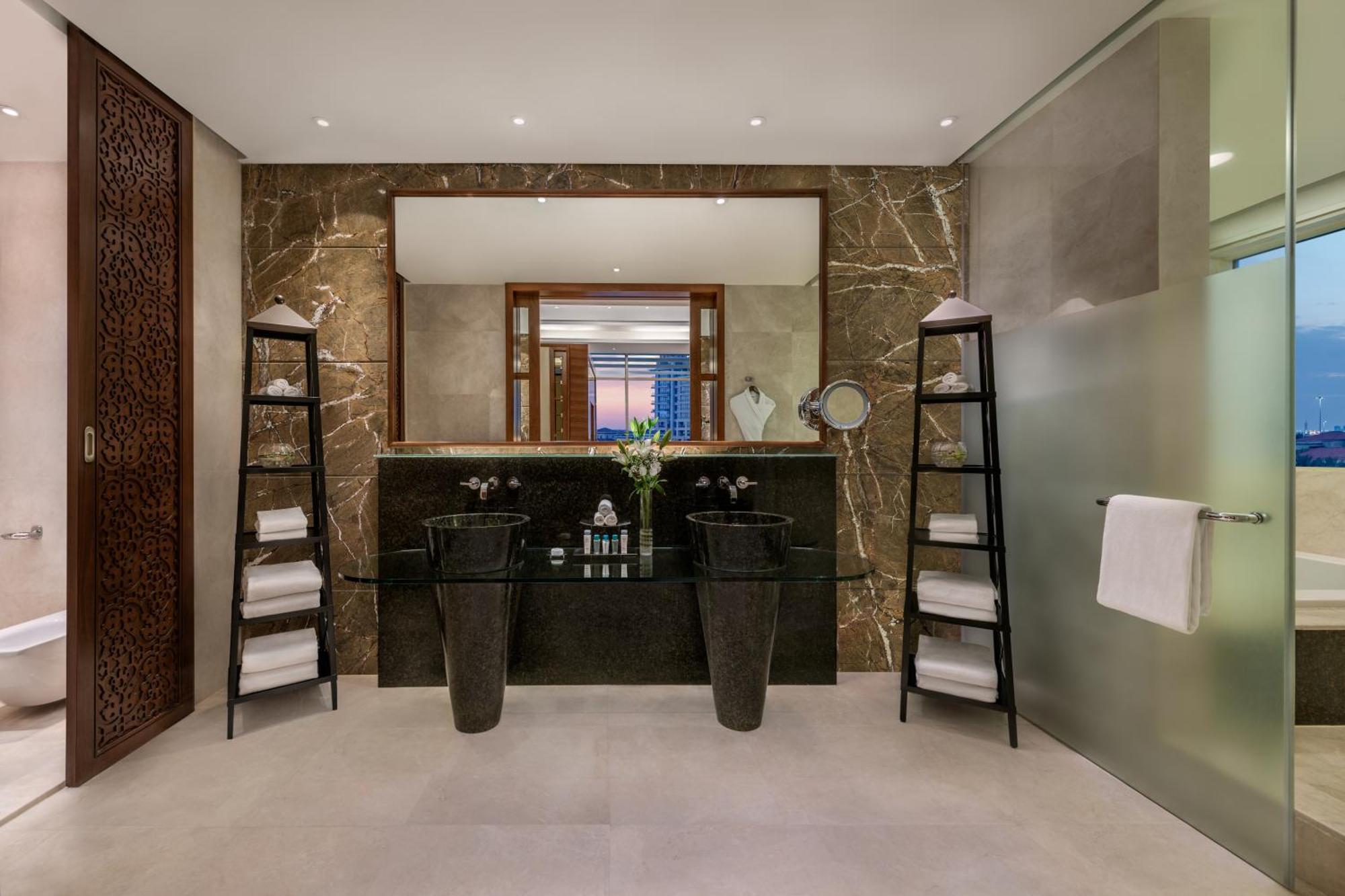 Al Raha Beach Resort & Spa Abu Dhabi Eksteriør bilde The photo shows a modern, elegant bathroom interior. It features a large mirror hanging above a double-sink vanity with a dark stone countertop. On either side of the vanity are tall, slender vases that might be holding decorative elements. There are