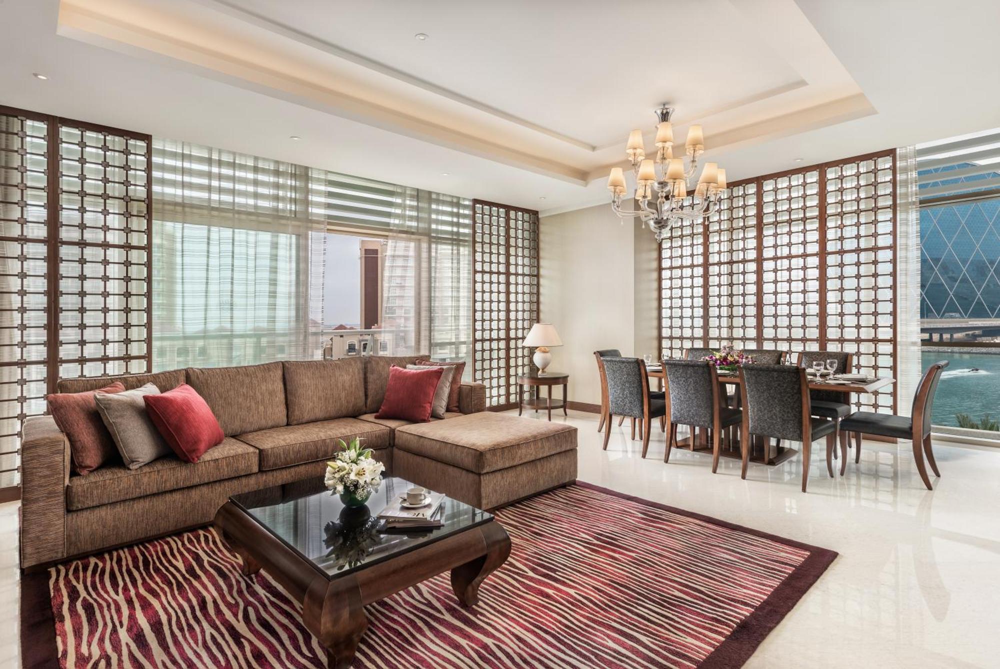 Al Raha Beach Resort & Spa Abu Dhabi Eksteriør bilde The photo shows a stylish and modern living space. On one side, there is a comfortable sectional sofa in a brown upholstery, accented with red and gray cushions. In front of the sofa, there is a glossy black coffee table adorned with a small floral a