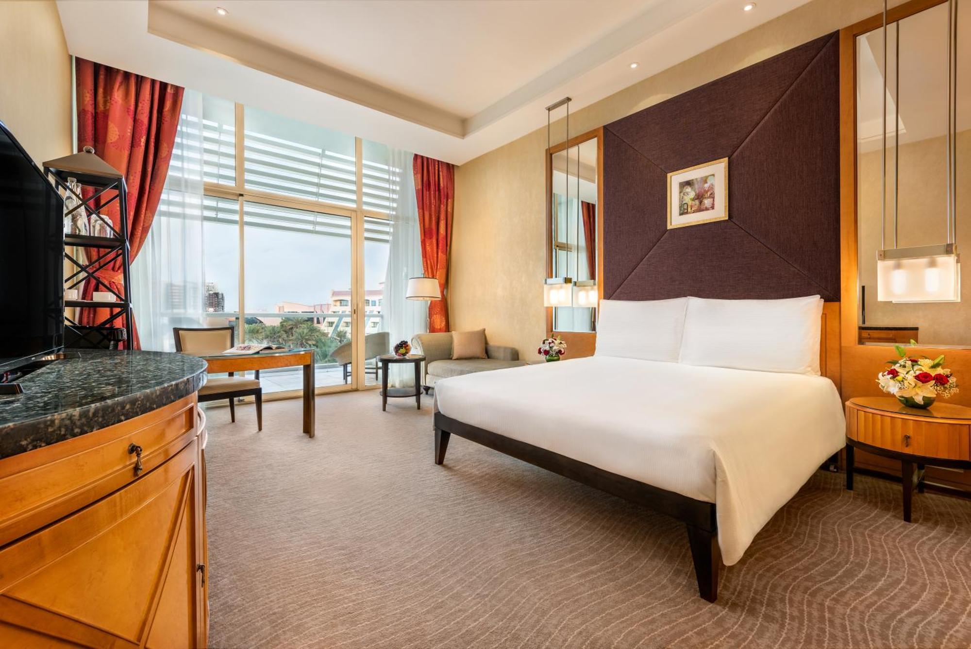 Al Raha Beach Resort & Spa Abu Dhabi Rom bilde The photo shows a modern hotel room featuring a large bed with a white duvet positioned against a purple accent wall. There are tall windows with sheer curtains allowing natural light to enter the space, along with red drapes framing the windows. A d