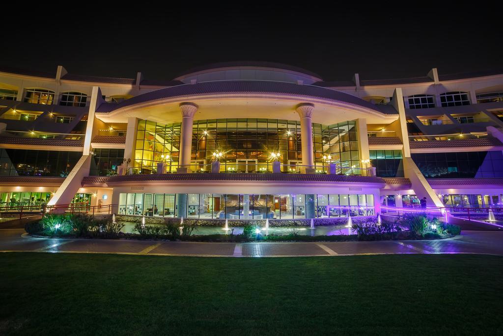 Al Raha Beach Resort & Spa Abu Dhabi Eksteriør bilde The photo shows a modern architectural building illuminated at night. The structure has a large central entrance with multiple glass windows, flanked by symmetrical columns. The exterior features a combination of sleek lines and curves, with lighting